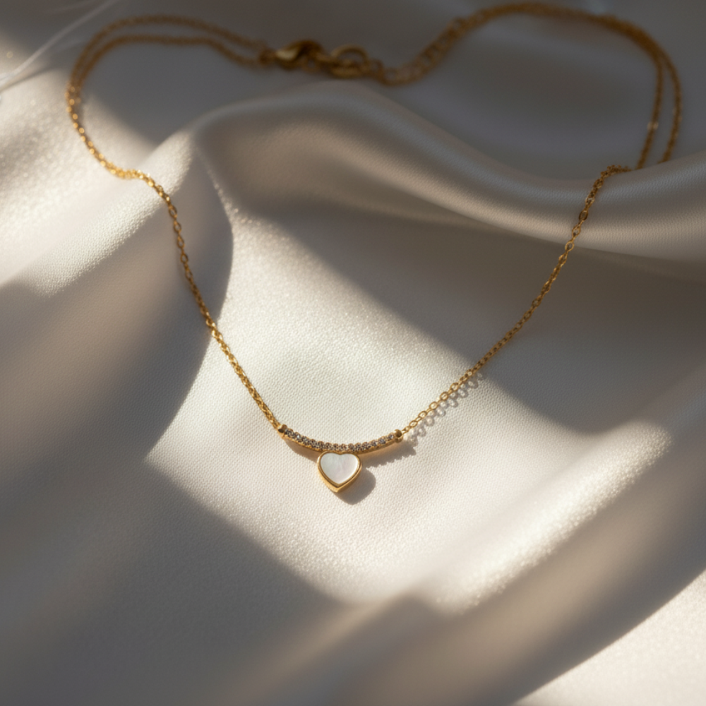 Gold necklace with white heart pendant placed on soft satin fabric under natural light