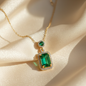 Gold chain necklace with emerald-cut green pendant on soft fabric background