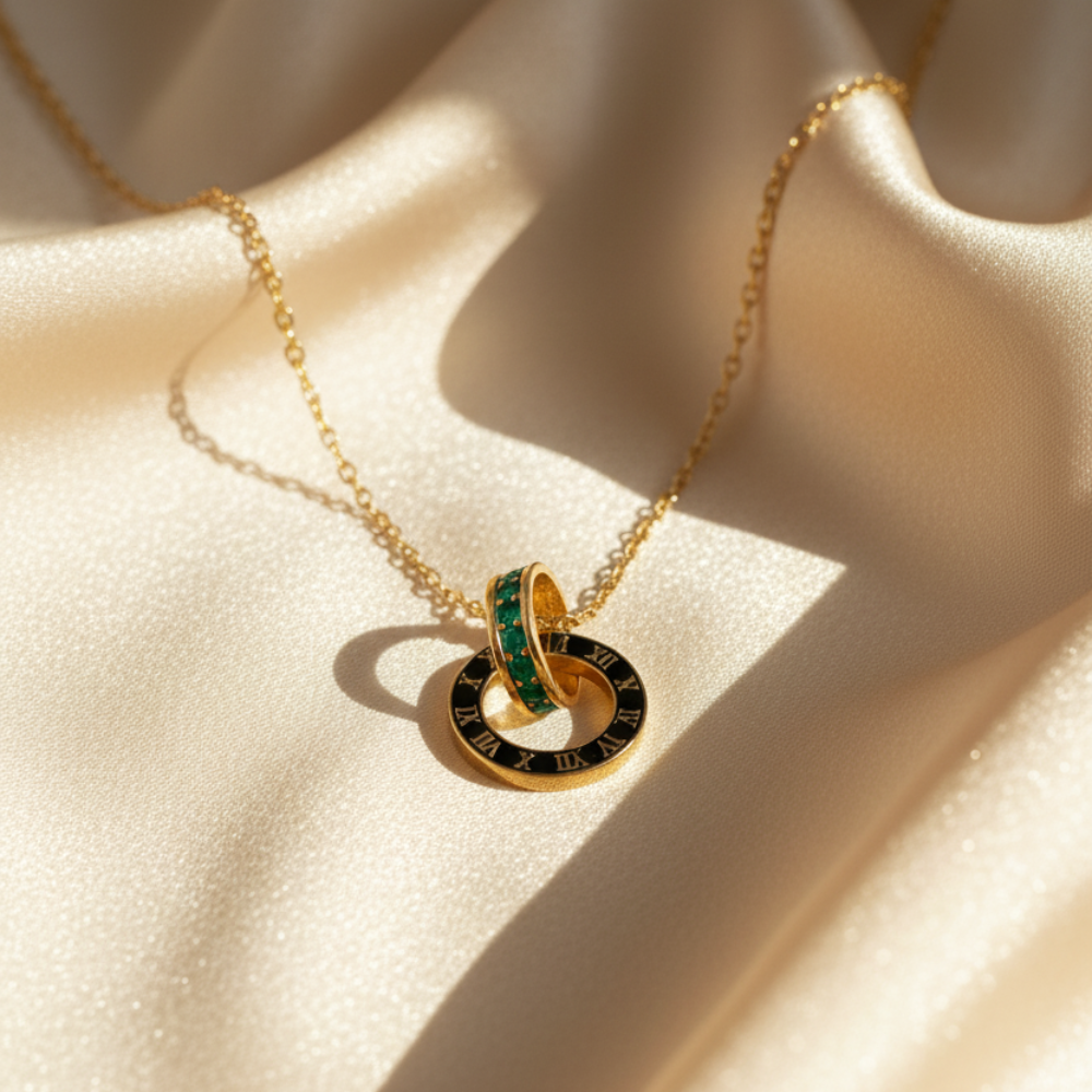 Gold Roman numeral necklace with emerald crystal ring placed on beige satin fabric