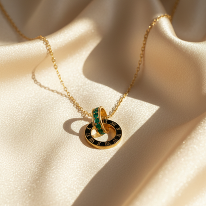 Gold Roman numeral necklace with emerald crystal ring placed on beige satin fabric