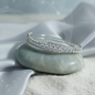 Silver crystal bangle bracelet displayed on a stone with soft blue background