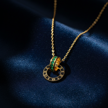 Gold Roman numeral pendant necklace with emerald stones on dark blue fabric background