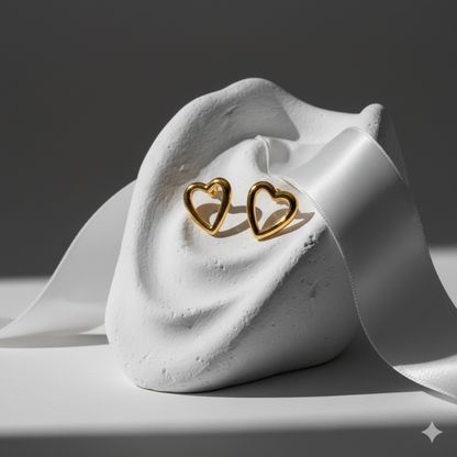 Gold heart stud earrings displayed on soft gray fabric