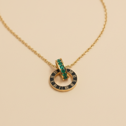 Close-up of gold Roman numeral necklace with emerald stone on peach background